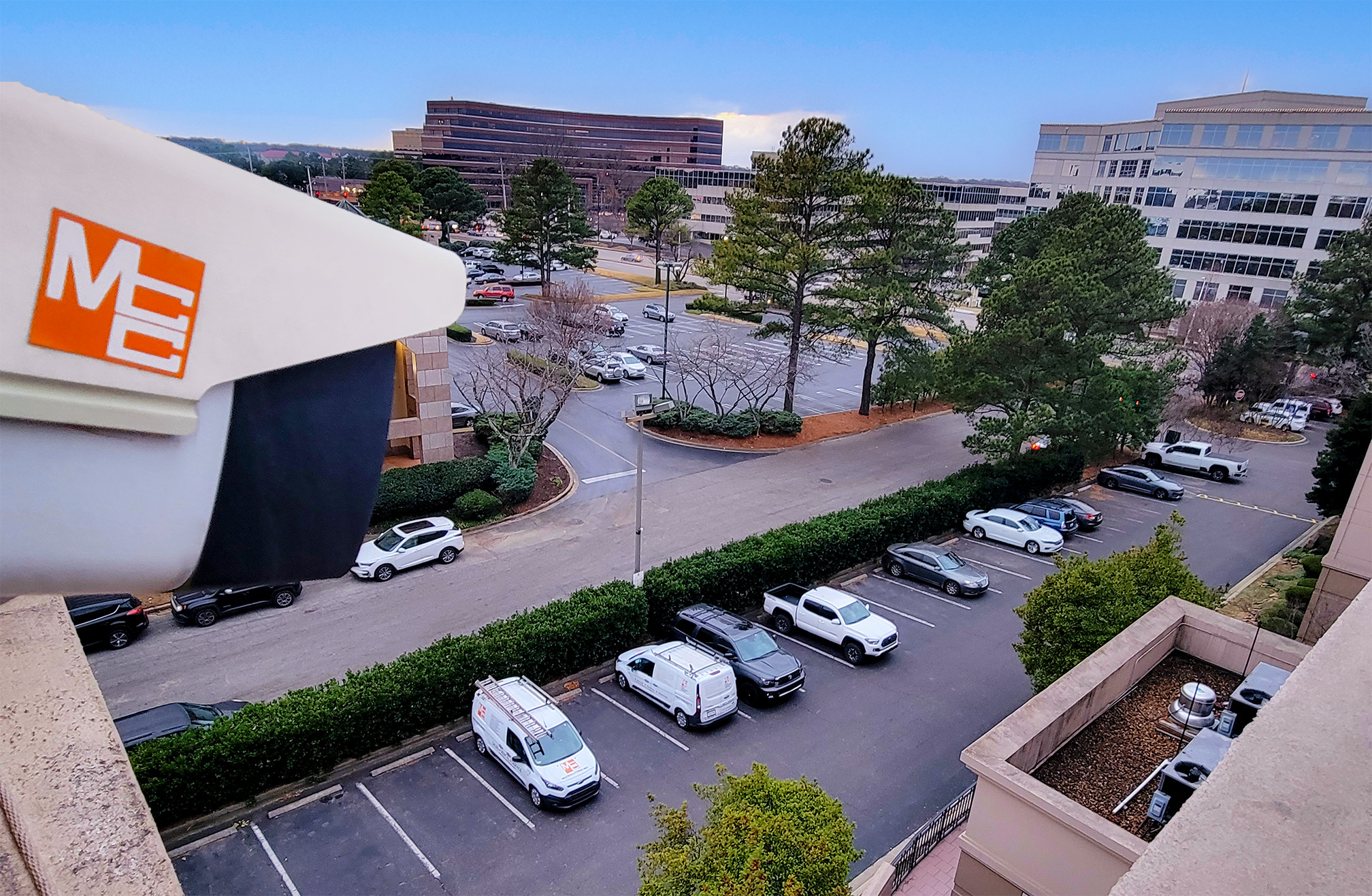 MCC CCTV Security Camera mounted to the top of a building overlooking a parking lot full of cars.