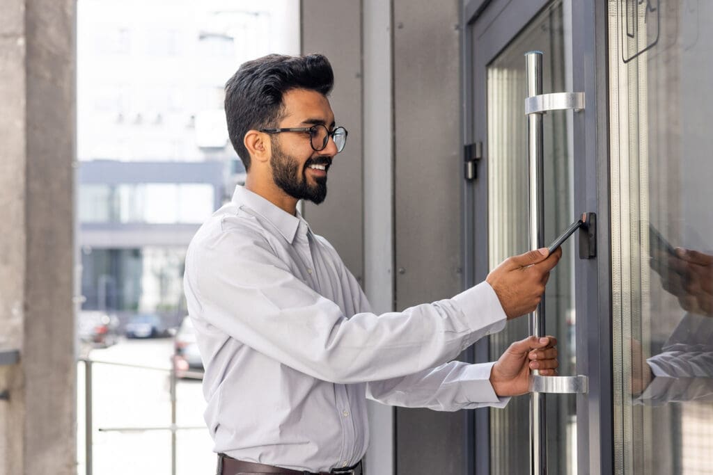 Young business man using his smartphone to open a commercial access control door lock - door card readers for business access control systems