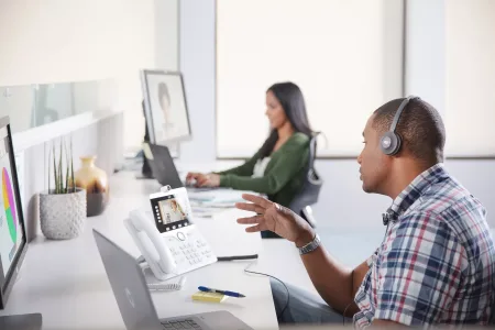 Two people at a desk on Webex video calls on their computers or Cisco desk phones demostrating the ease of Webex collaboration solutions.
