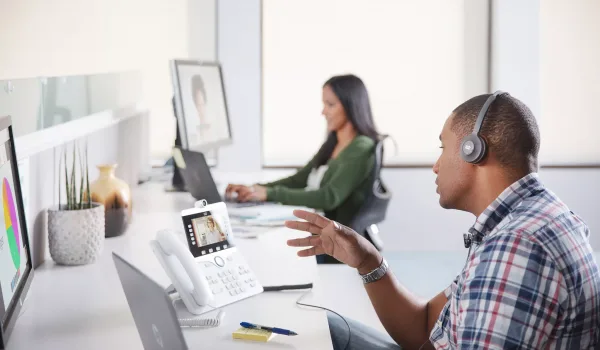 Two people at a desk on Webex video calls on their computers or Cisco desk phones demostrating the ease of Webex collaboration solutions.