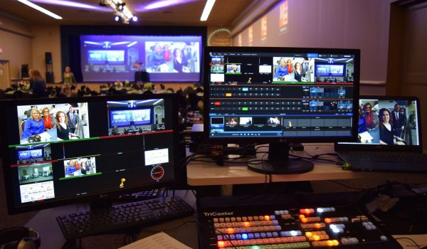 Image displaying multiple computer screens in the foreground, each showing various aspects of the NewTek Tricaster video production system. The screens reveal intricate details of the software's interface, demonstrating its complex functionality and capabilities in managing real-time video production.