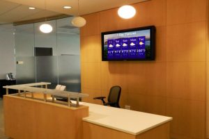 MCC Digital Signage display on a wall behind the reception area of an office.