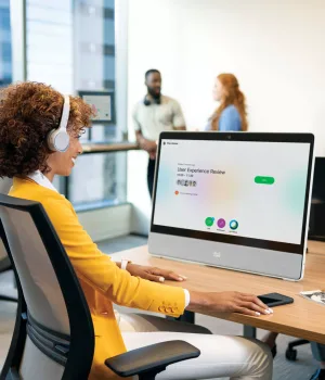 Woman sitting at a desk infront of the Cisco Webex Desk Pro and wearing Cisco bluetooth headphones getting ready to join a Webex meeting. Modern business phone system setup with Webex Calling interface