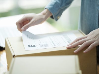 Hands place a printed document with a barcode into an open cardboard box.