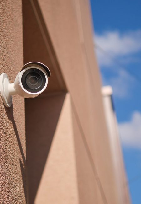 Outdoor security camera mounted on a textured beige wall, angled downward to monitor the area.