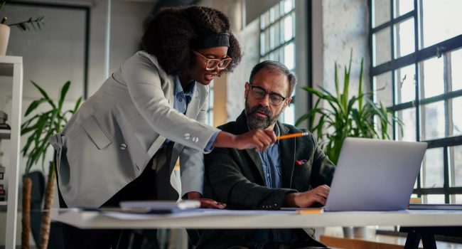 Two professional business individuals engaging in a productive discussion over a computer, exploring the practical benefits and efficiency of using a document management software. This scene exemplifies the transformative power of document management systems and workflow automation in the modern business environment.