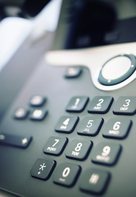 Close-up of a desk phone keypad with a hand lifting the handset to answer a call.