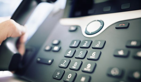Close-up of a desk phone keypad with a hand lifting the handset to answer a call.