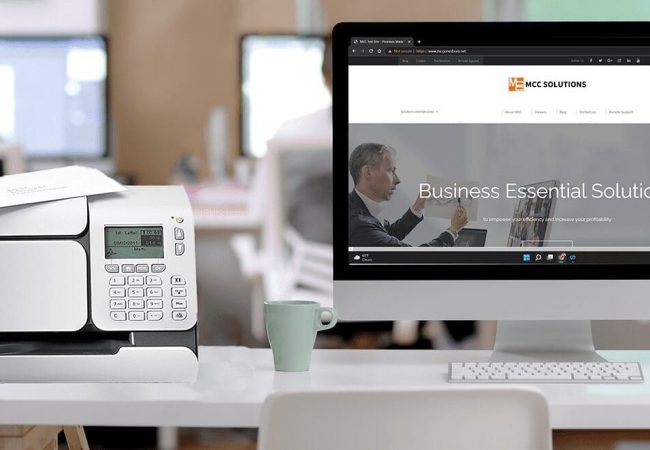 MCC Solutions postage meter page header - Quadient postage meter sitting on a desk with a computer monitor showing the MCC Solutions website