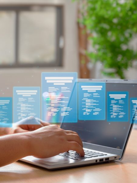 Hands on a laptop keyboard with floating blue document icons above the screen, suggesting digital data processing.