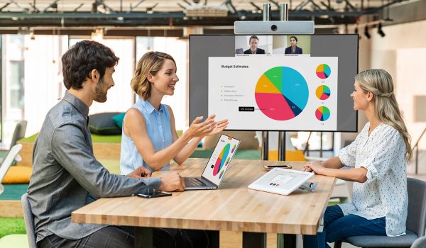 Three people in an office sitting around a table having a video conference business meeting on a Webex Room Board.