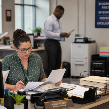 Busy school office with multiple people milling about.