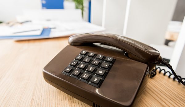 Brown landline telephone on a wooden desk with a coiled cord, in an office setting.