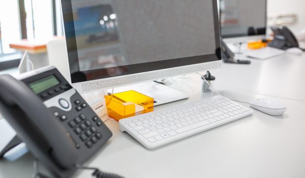 Office workspace with a desktop computer, keyboard, mouse, and a bright orange desk organizer on a white desk.
