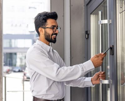 Young business man using his smartphone to open a commercial access control door lock - door card readers for business access control systems