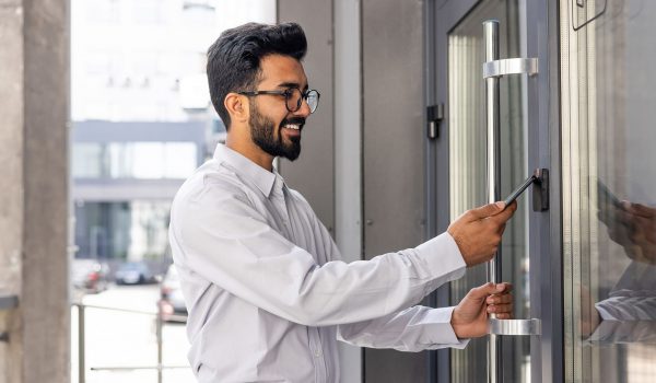 Young business man using his smartphone to open a commercial access control door lock - door card readers for business access control systems