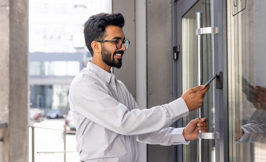 Young business man using his smartphone to open a commercial access control door lock - door card readers for business access control systems