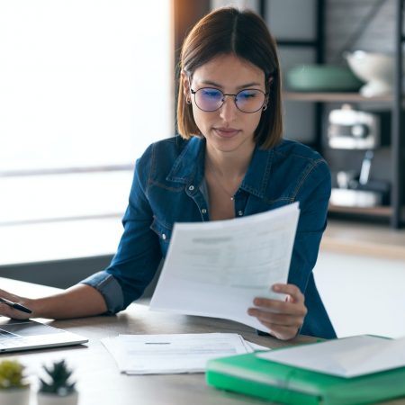young woman working with computer while consulting some invoices and documents in the kitchen. Image for AP Automation pages of the Document Solutions section of the MCC website